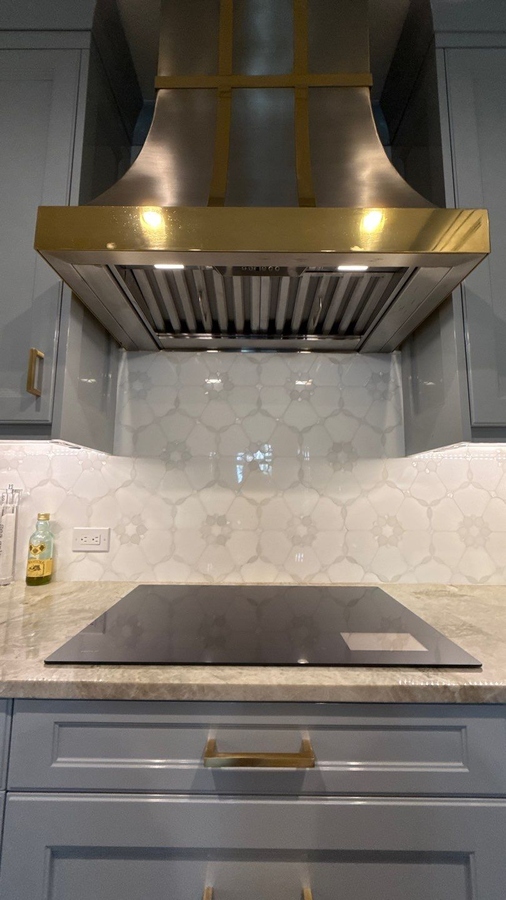 Close-up of brass-accented range hood and detailed tile backsplash in San Antonio kitchen remod