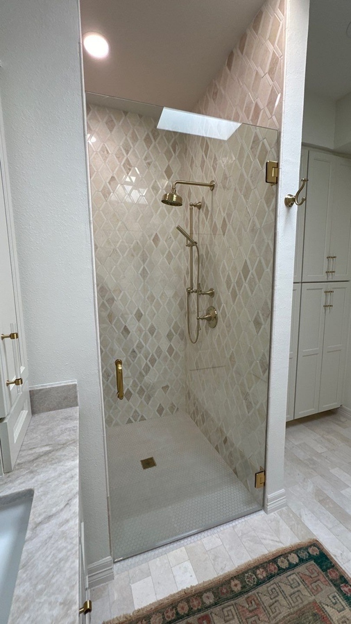 Glass-enclosed shower with geometric tilework and gold hardware in Castle Hills, TX by Wade Cal