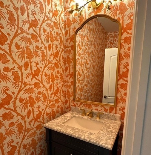 Vibrant powder room with orange botanical wallpaper and gold mirror in Olmos Park, TX by Wade C